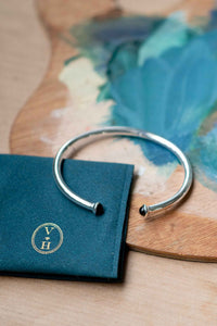 Silver bracelet with black accents on teal pouch