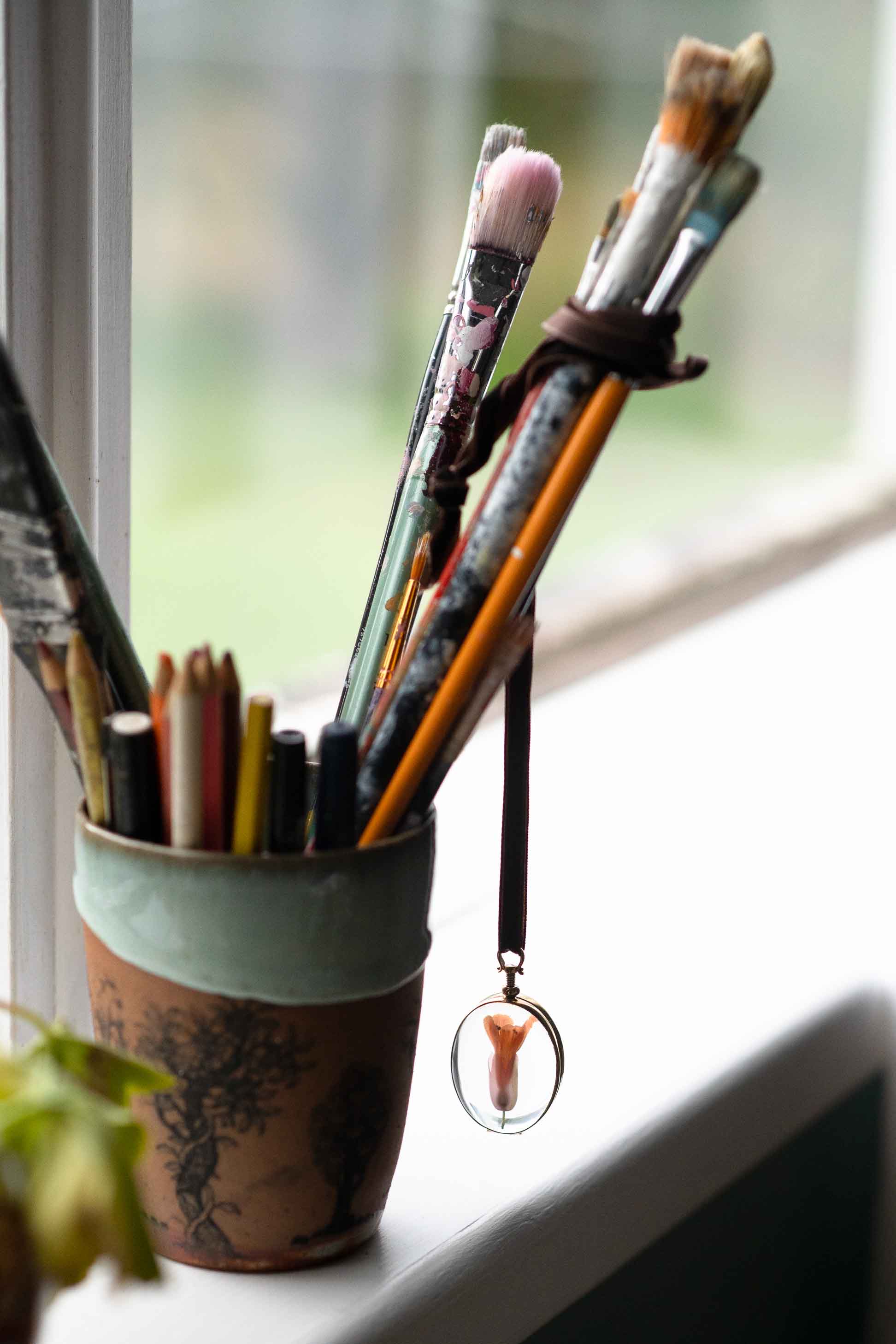 Crystal locket oval charm with artist's paintbrushes in a cup.