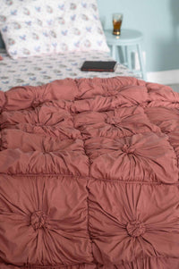 Dusty rose tufted bedspread with patterned pillow & bedside table