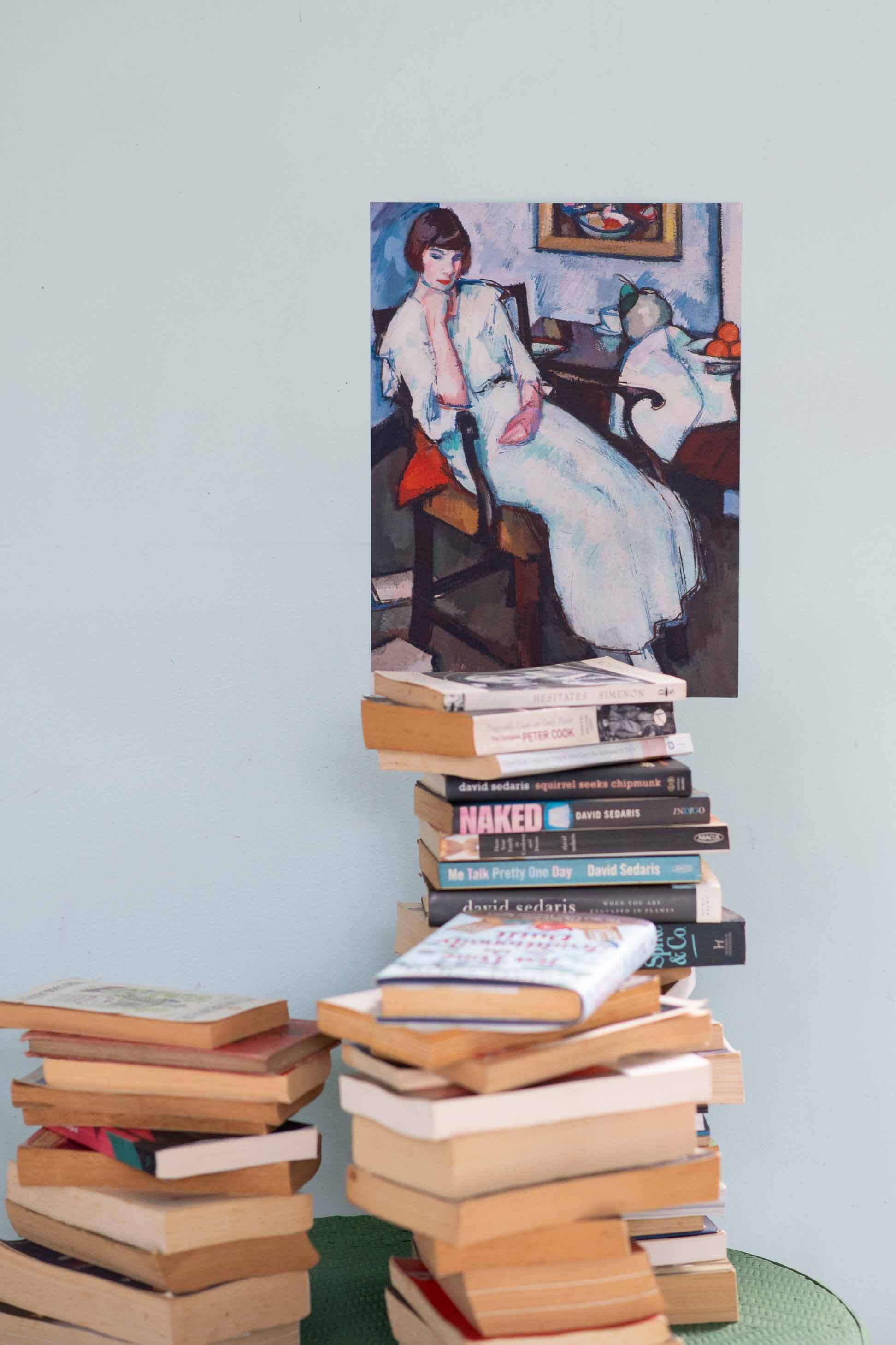 Girl in white painting above stacked books.