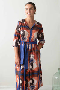 Woman in patterned dress with blue sash.