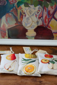 Scented sachets with fruit designs and a vase in the background
