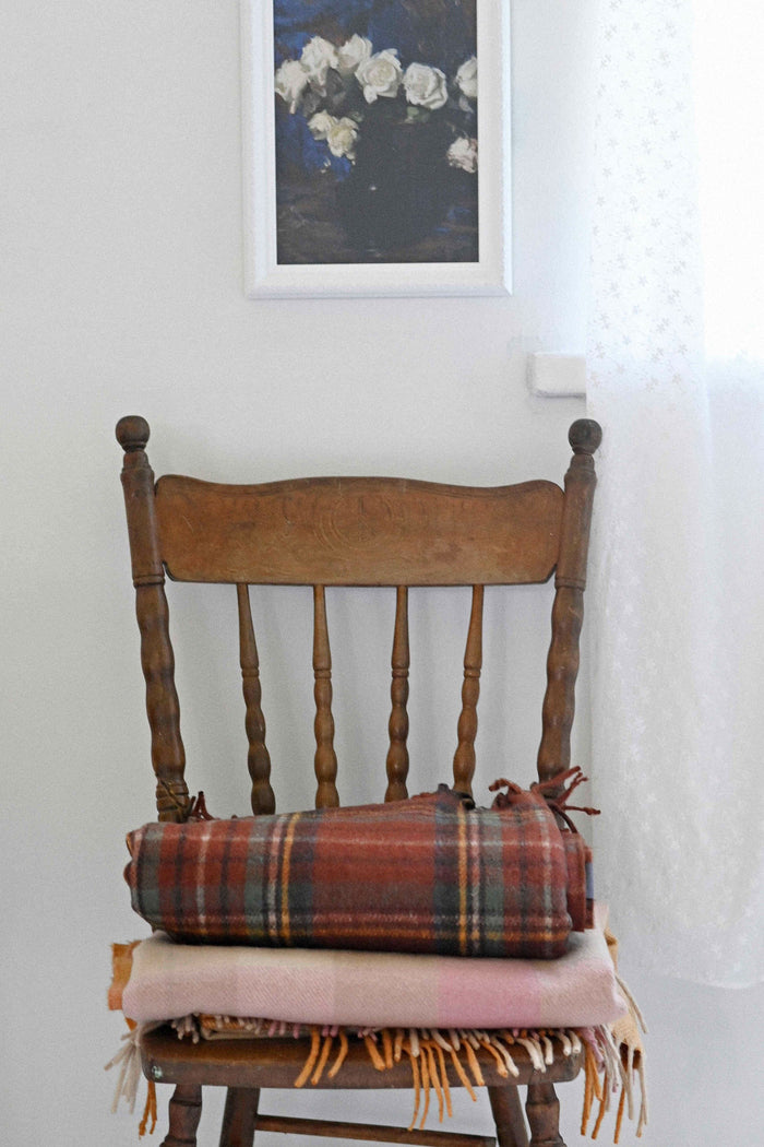 Art print of white roses above a chair with orange gingham blanket.