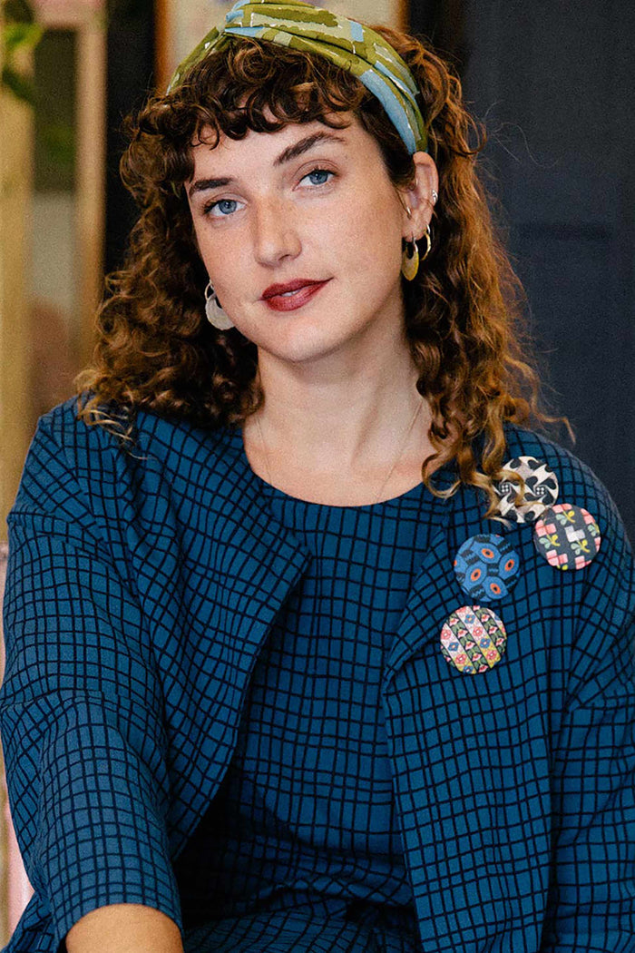 Woman in petrol blue jacket with brooches and turban.