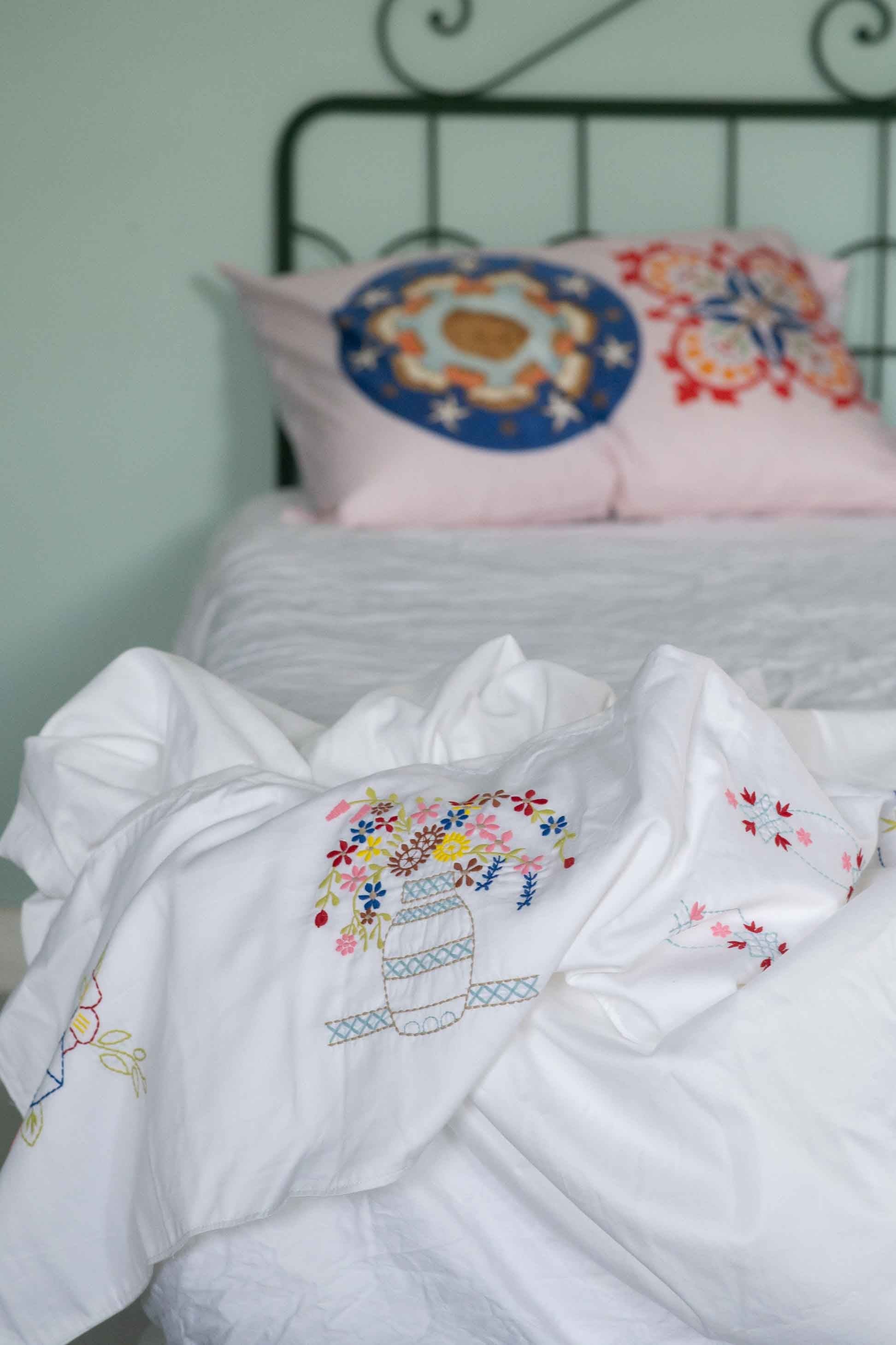 Embroidered bedding with decorative pillows on a bed frame, DSC4686