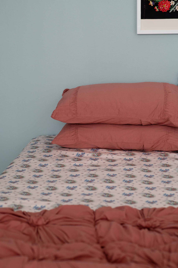 Bedroom with pink bedding and patterned sheets.