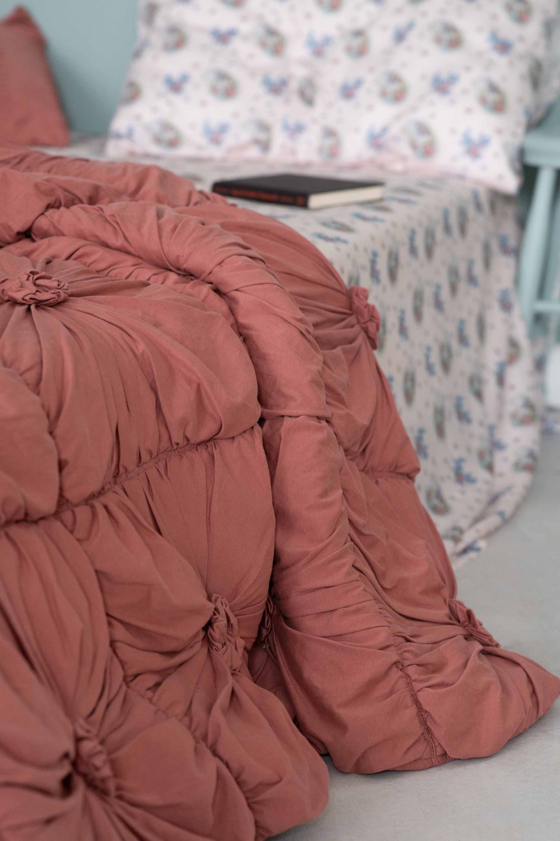 Pink ruched comforter on bed with book