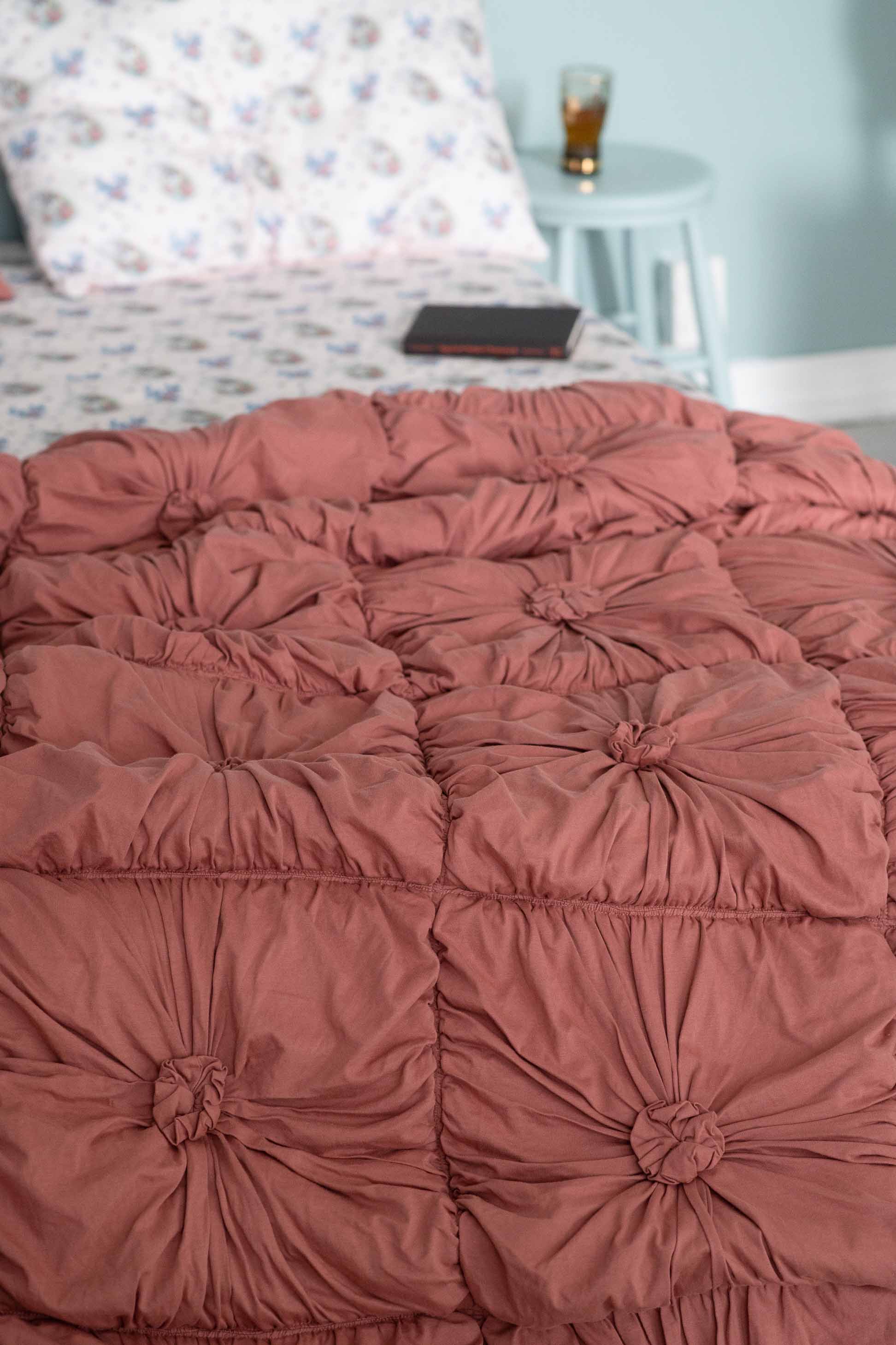 Dusty rose tufted bedspread with patterned pillow & bedside table