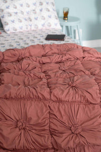 Dusty rose tufted bedspread with patterned pillow & bedside table