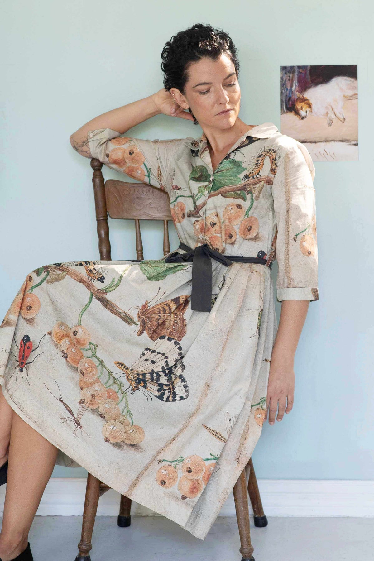 Gianna in insect print dress seated on chair.