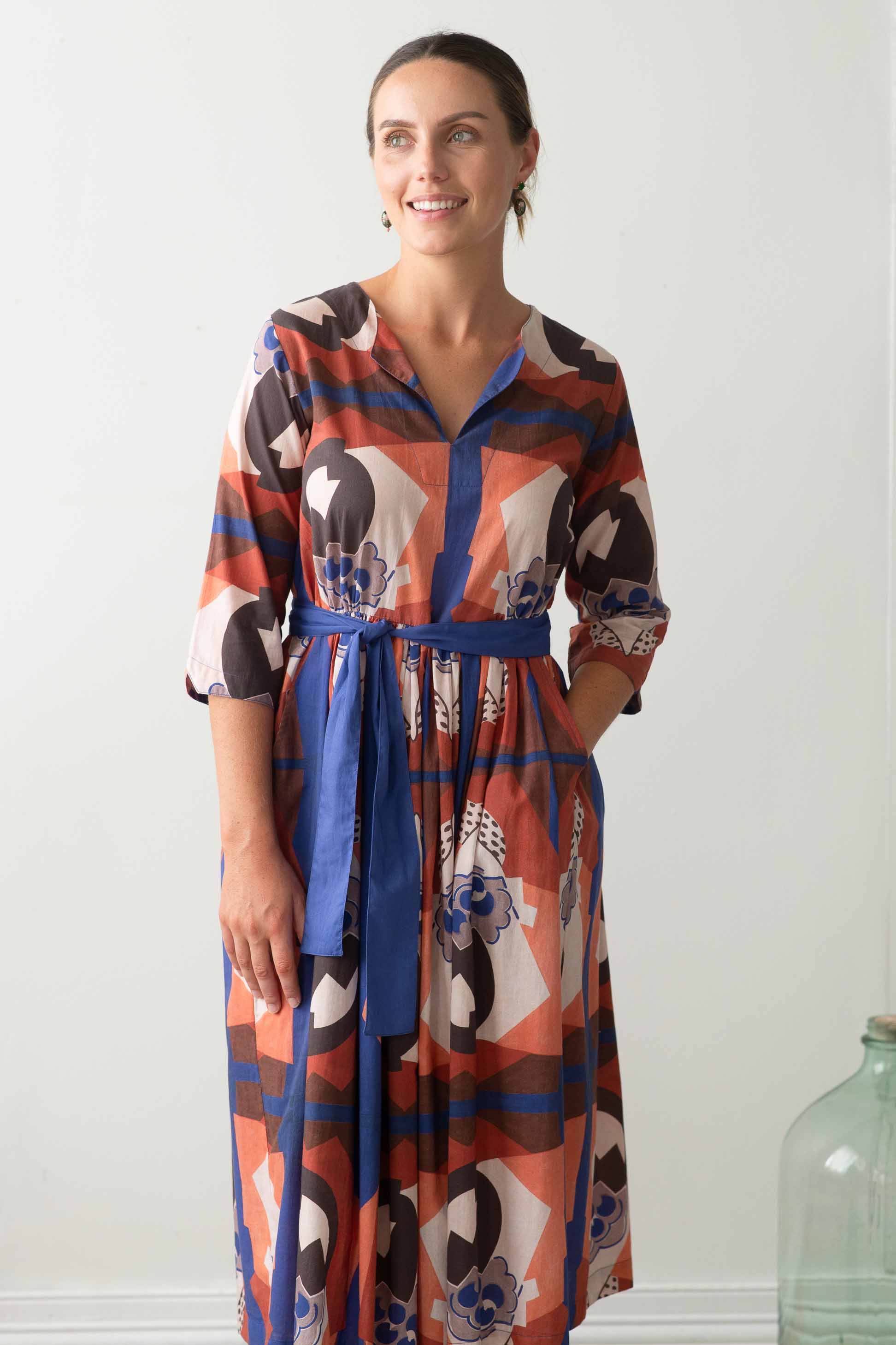 Woman in patterned dress with blue sash.