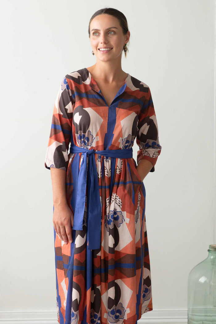 Woman in patterned dress with blue sash.