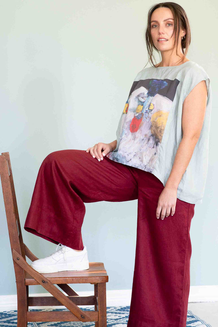 Woman in red pants and Peggy Still Life shirt, leaning on chair.