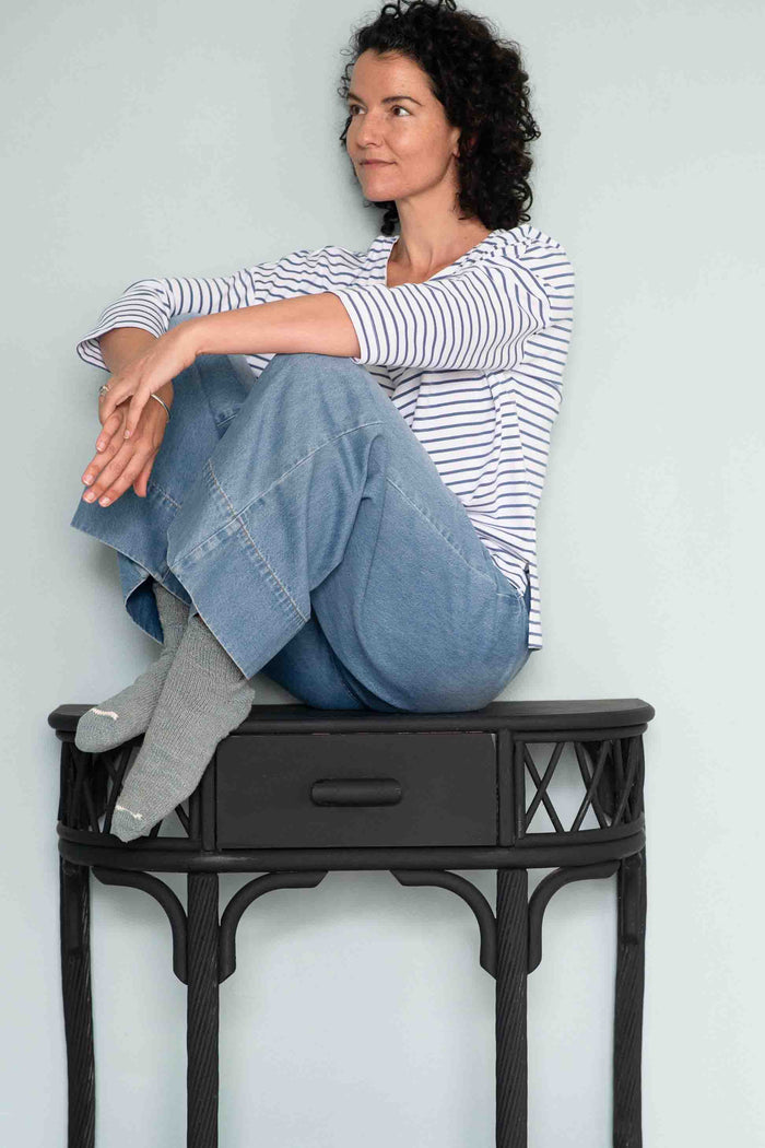 Woman in Solent tee, denim jeans, Garabou socks, bracelet, sitting on black...